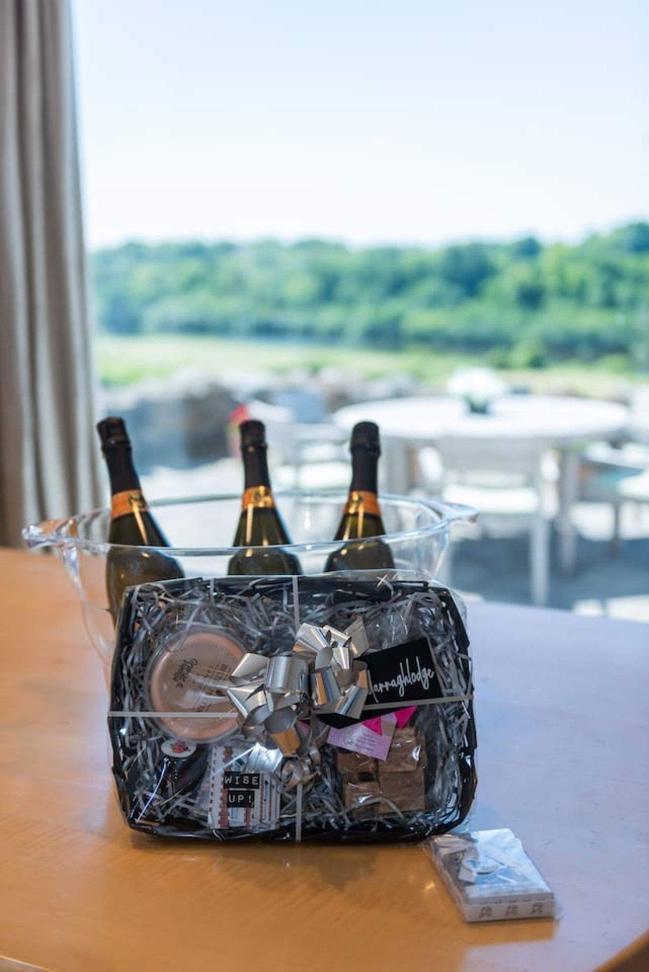 A glass container with three bottles of wine, a wrapped gift, and a small box on a table.