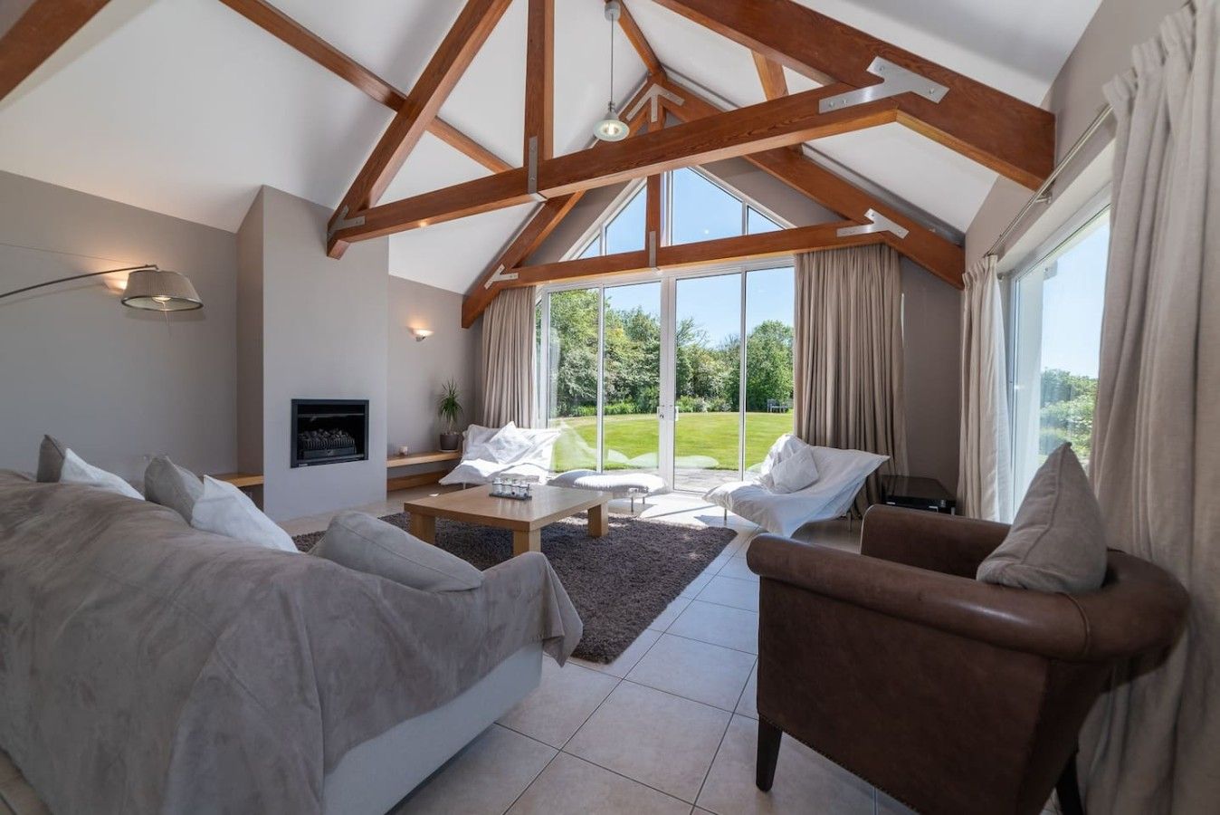 A spacious room with a high ceiling, a fireplace, a large window, and a view of the outdoors.