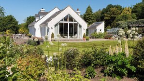 A white house with a large glass door and a well-maintained garden with various plants and flowers.