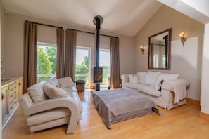 A spacious living room with a fireplace, two sofas, a coffee table, and a large window offering a view of greenery. - Stunning North Coast Villa, River View Hot Tub 20+ (Coleraine)