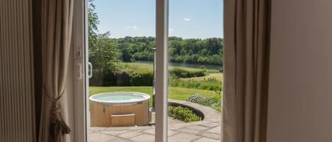 A view through a glass door to an outdoor hot tub area with a lawn and trees in the background.