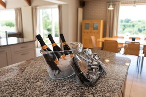 A kitchen counter with a glass ice bucket containing bottles, a wrapped gift, and ice. - Stunning North Coast Villa, River View Hot Tub 20+ (Coleraine)