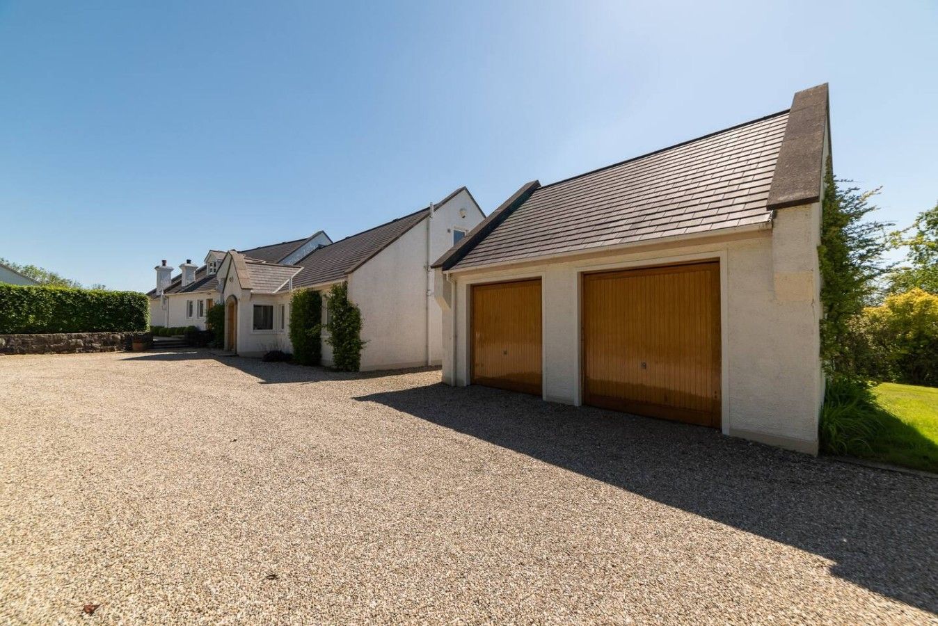 A row of detached houses with individual garages, a gravel driveway, and a clear sky.