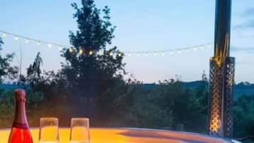 Un bain à remous avec un revêtement extérieur en bois, entouré d’arbres et illuminé de guirlandes lumineuses.