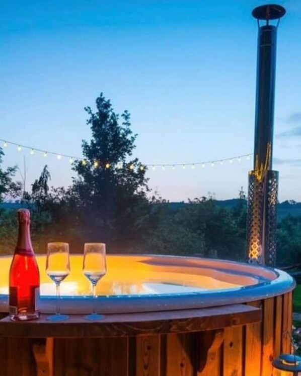 Un jacuzzi con revestimiento de madera, rodeado de árboles y luces colgantes.