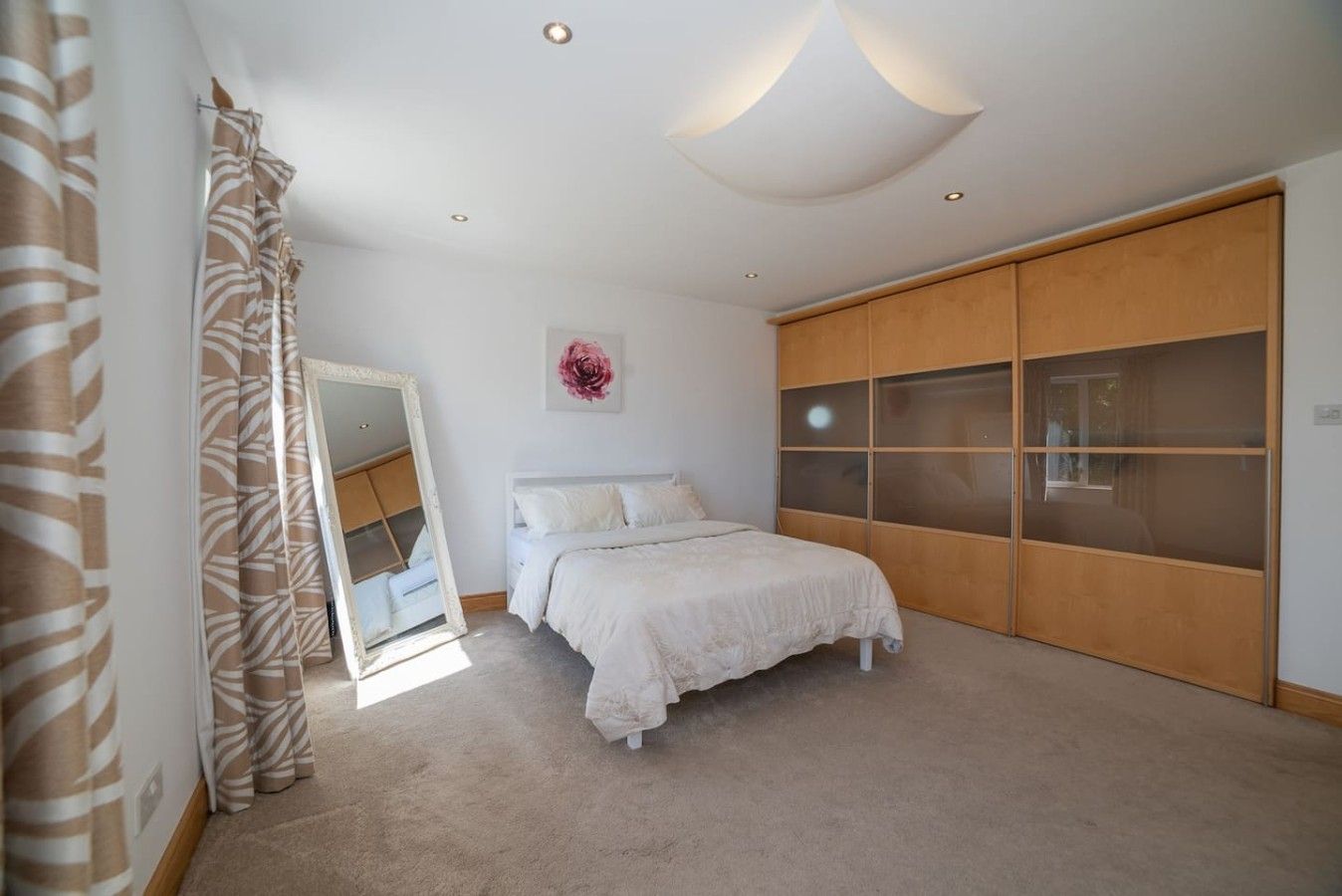A bedroom with a bed, a large mirror, a wardrobe, and a ceiling light fixture.