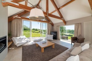 Un salon spacieux avec un haut plafond, une cheminée, un téléviseur et une grande fenêtre donnant sur un paysage verdoyant.