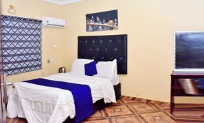 Habitació d'hotel amb un llit, aire condicionat fixat a la paret, un quadre de paisatge urbà i una televisió.