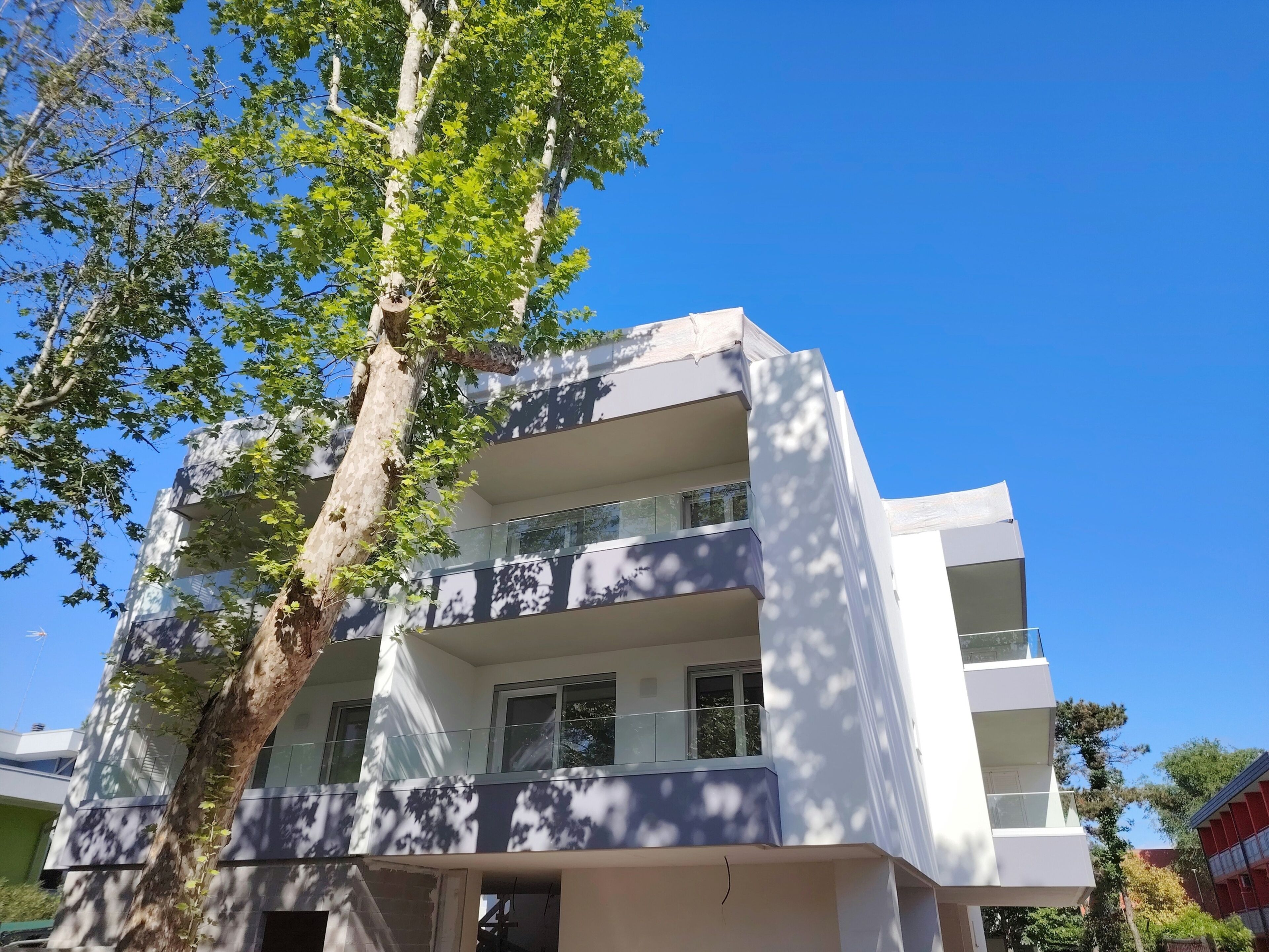 Un edificio de varios pisos con balcones y ventanas amplias, rodeado de árboles.