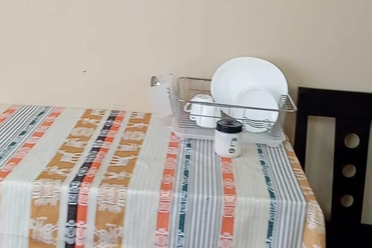 A TV mounted on the wall, a table with a patterned tablecloth, and a chair.