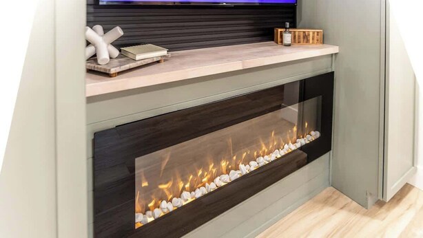 Una chimenea moderna con frente de vidrio, un televisor de pantalla plana arriba y un estante de madera con objetos decorativos.