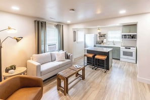 A modern living room with a sofa, a wooden coffee table, and a kitchen area with a dining table and bar stools.