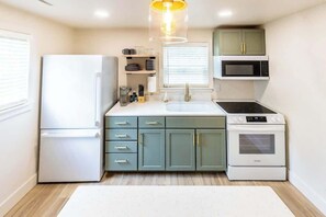 A compact kitchen with a refrigerator, microwave, stove, and sink.