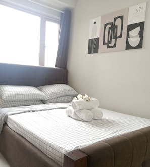 Un lit bien fait, avec une couverture à carreaux, des oreillers et une serviette enroulée décorée de fleurs.
