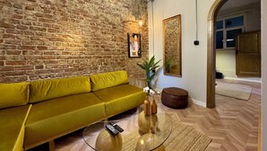 Una sala de estar con pared de ladrillo, un sofá amarillo, una mesa de centro de vidrio y piso de madera.