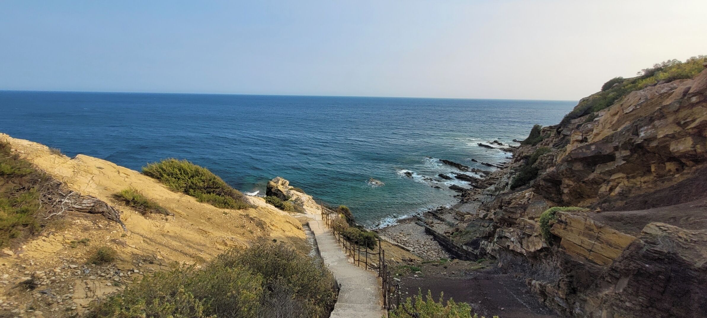 Un sendero costero que lleva a una costa rocosa con vistas claras al mar.