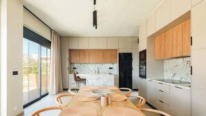 Une cuisine moderne avec des meubles en bois, un plan de travail en marbre et un coin repas comprenant une table et des chaises en bois.