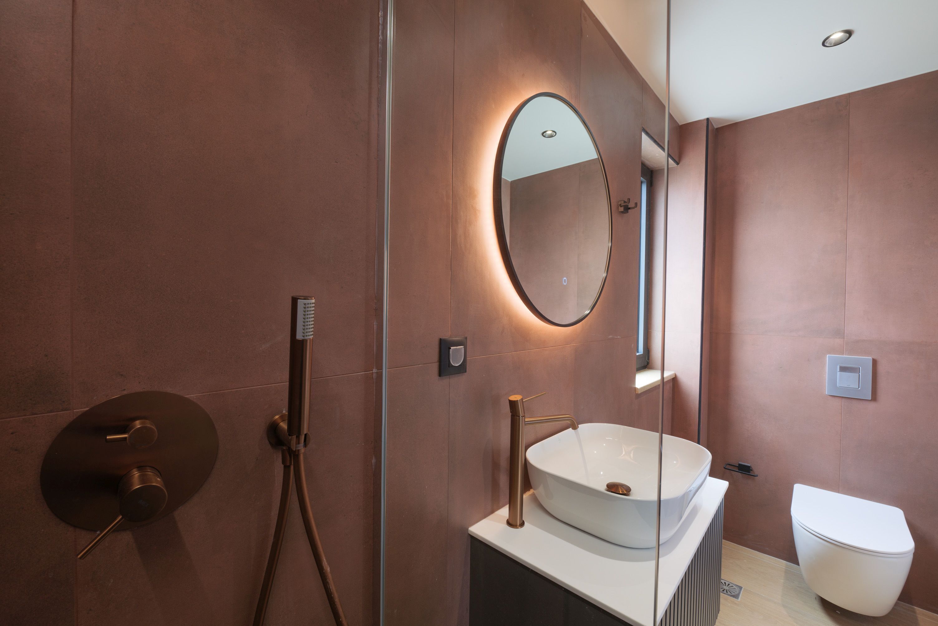 Une salle de bain moderne avec un grand miroir ovale, un lavabo sur colonne et des toilettes.