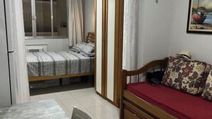 A compact living space with a dining table, a sofa, a wardrobe, and a bed with patterned bedding. - Apartment with side sea view, post 5 (Copacabana)