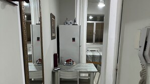 A narrow hallway with a white tiled floor, a white table with chairs, a refrigerator, and a telephone. - Apartment with side sea view, post 5 (Copacabana)
