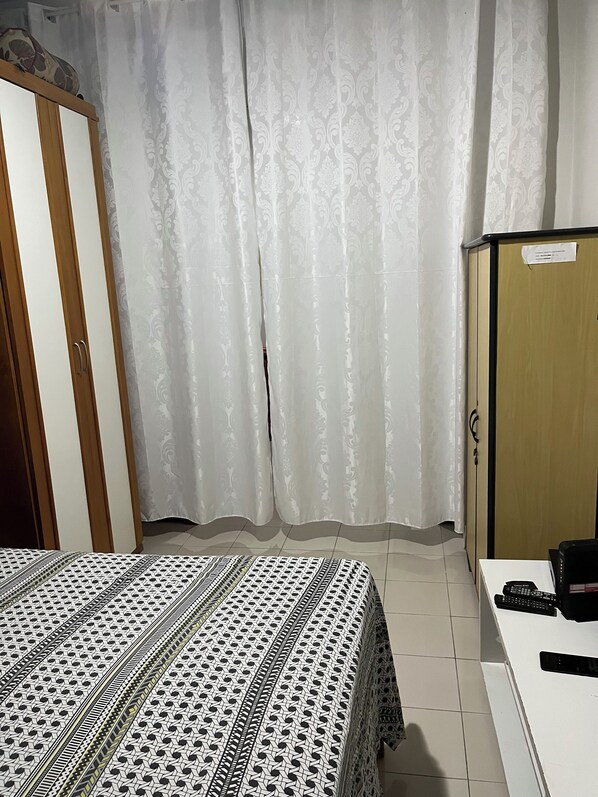 A bedroom with a bed, a wardrobe, a desk with a computer, and a curtain.