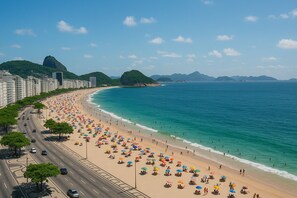 A beach with a road parallel to it, lined with trees and buildings.