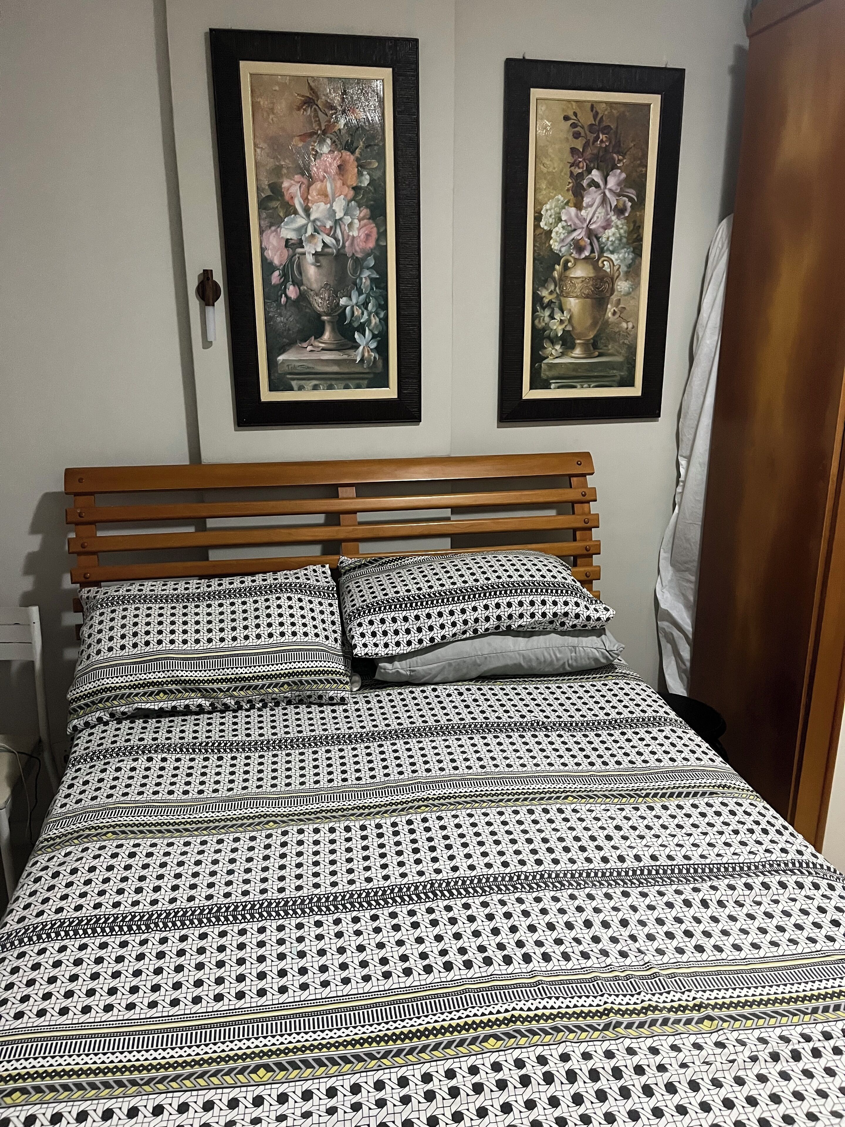 Una cama bien tendida con ropa de cama estampada, un cabecero de madera y dos cuadros con motivos florales en la pared.