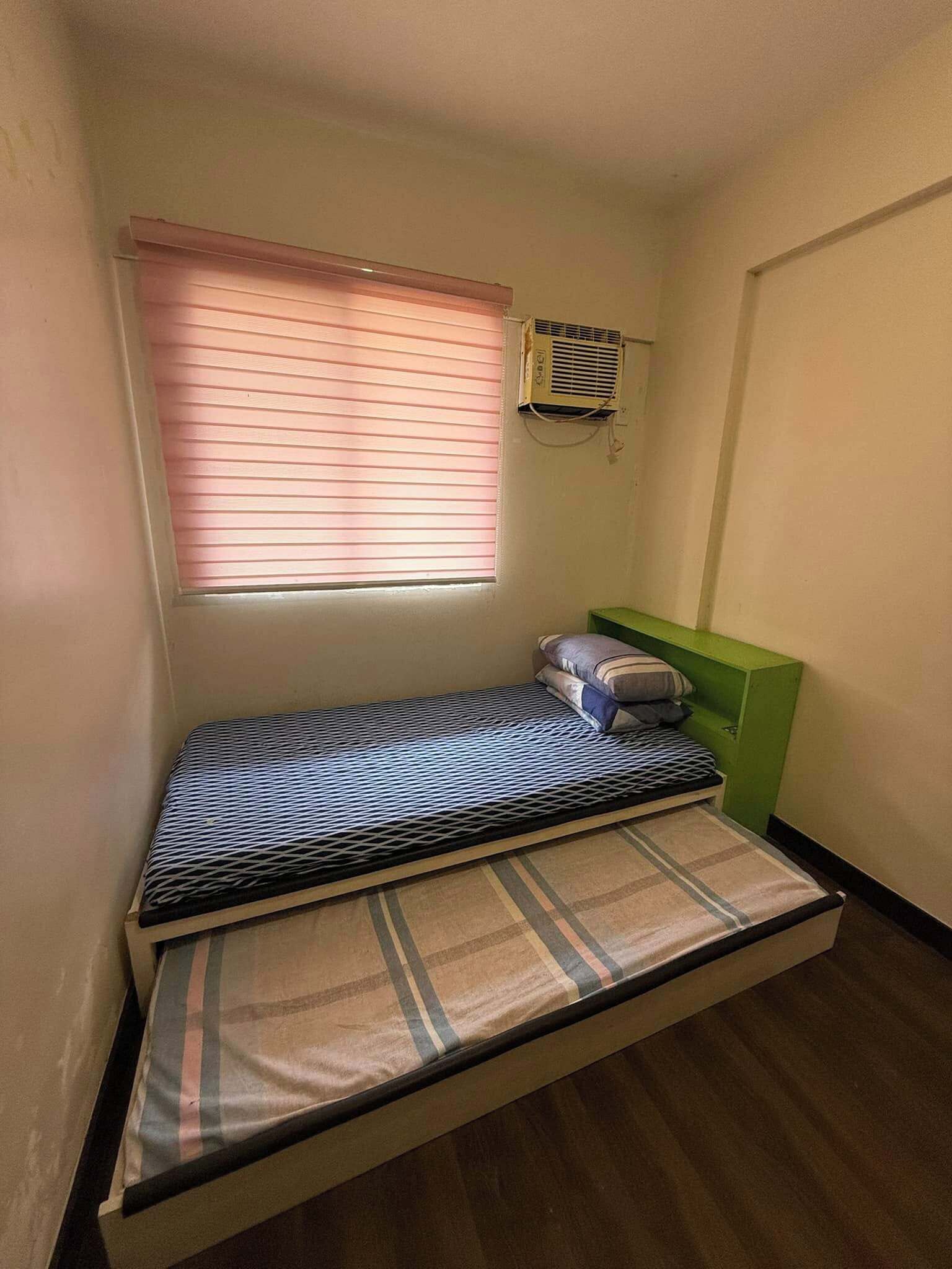 Une petite chambre avec un lit simple, une fenêtre, un appareil de climatisation et une tête de lit verte.