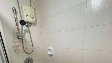 Ett litet, kaklat duschutrymme med ett handhållet duschmunstycke, en väggmonterad kontrollpanel och en gul hink på golvet.