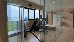 A gym with cardio equipment and a water dispenser, large windows with a view, and a glass partition. - Hotel Makkan Boca (Boca del Río)