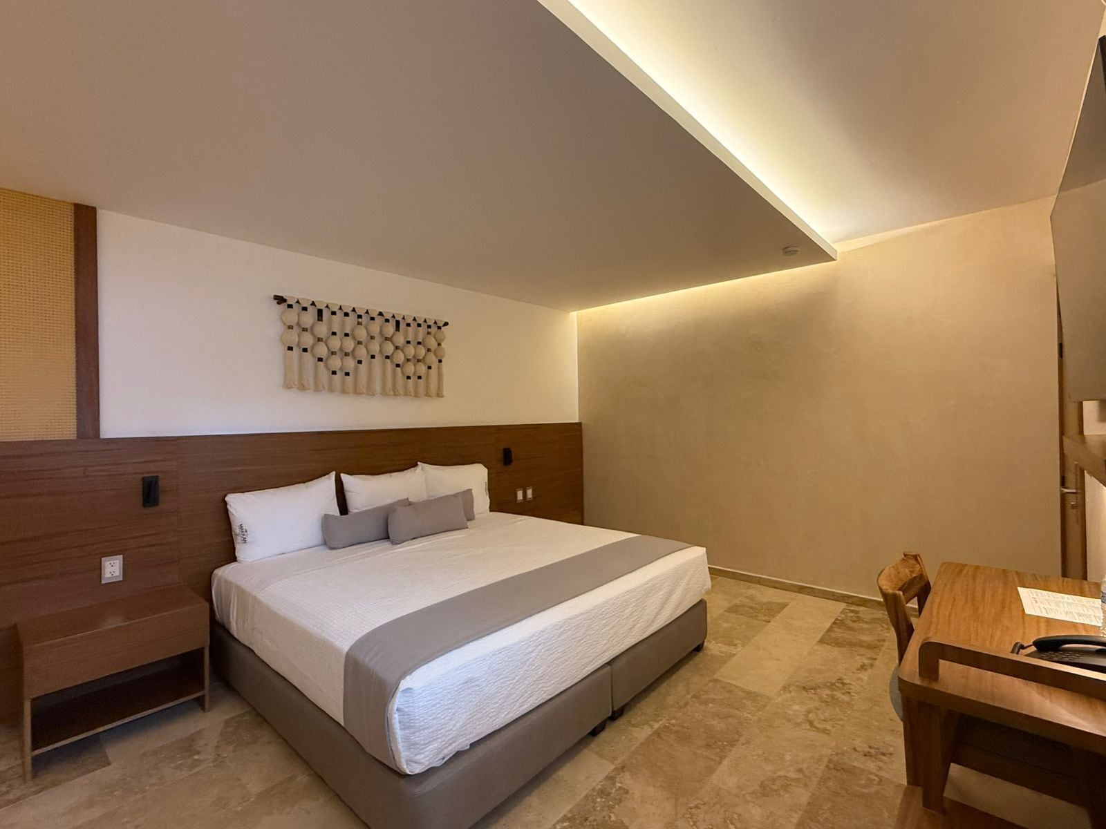 Une chambre d’hôtel moderne avec un grand lit, une table de chevet en bois, un bureau et un élément décoratif fixé au mur.