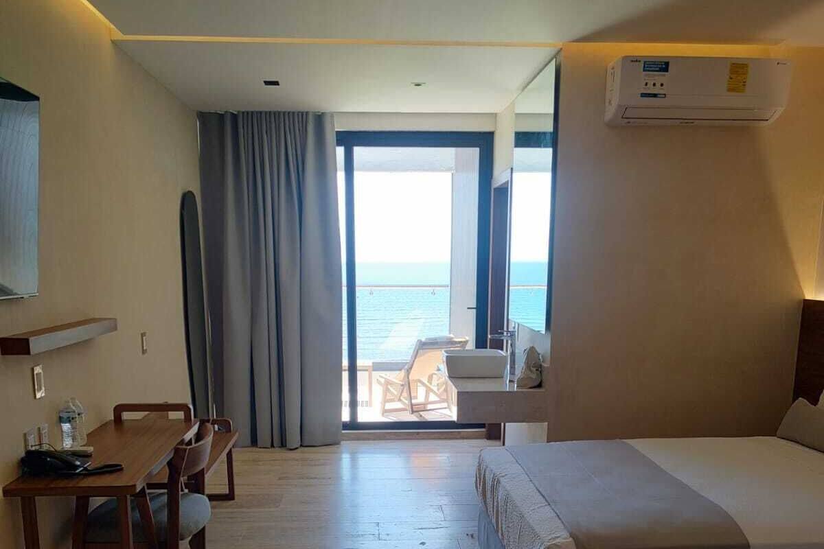 Habitación de hotel con cama, escritorio y silla. Se ve el mar a través de un ventanal grande.