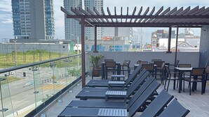 A rooftop lounge area with sun loungers and tables, overlooking a cityscape with tall buildings. - Hotel Makkan Boca (Boca del Río)