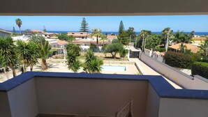 Ein Balkon mit Blick auf eine Wohngegend, ein Schwimmbad und das Meer.
