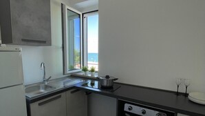 Une cuisine compacte équipée d’un évier, d’une cuisinière et d’une fenêtre donnant sur la mer.