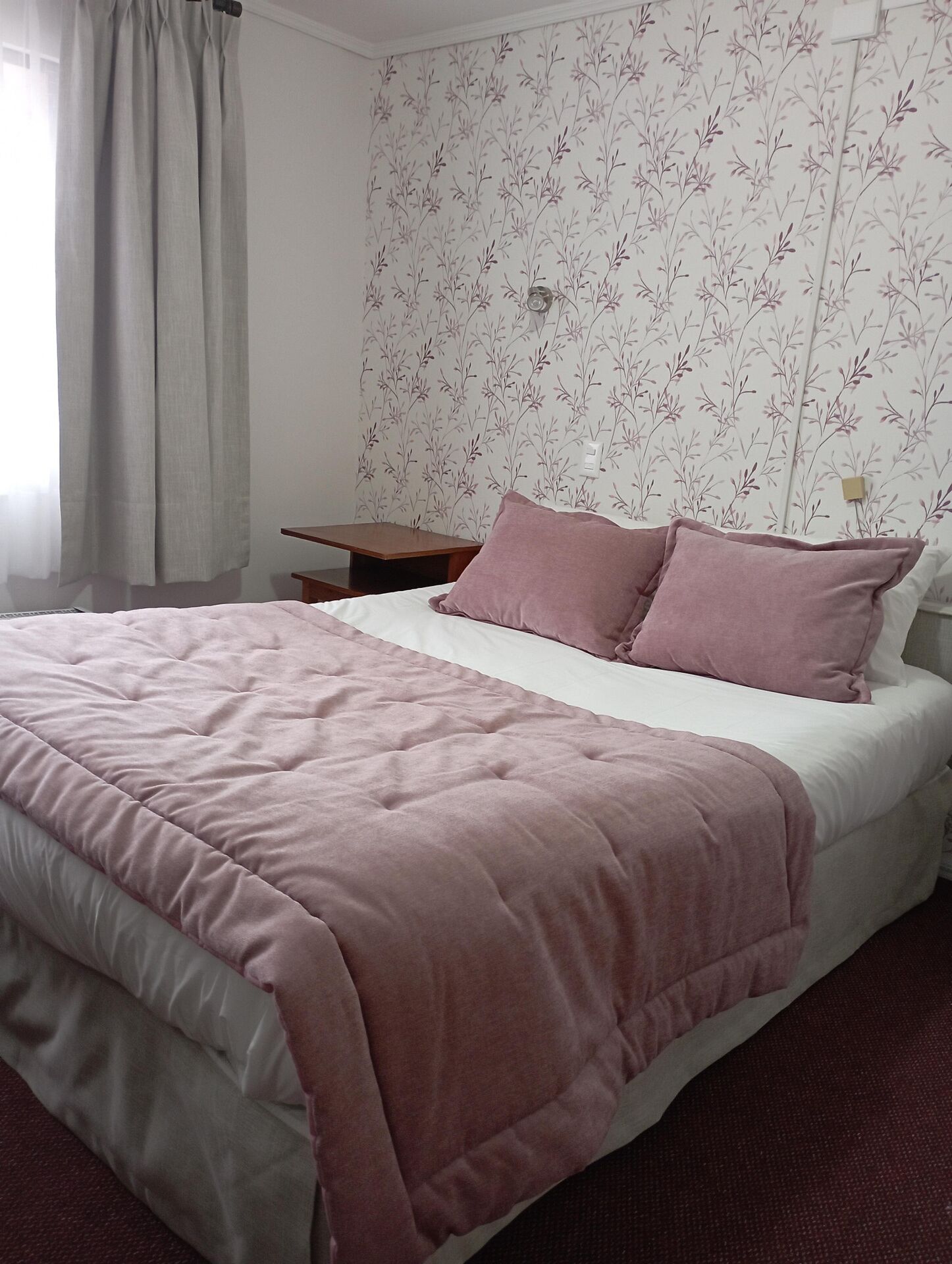 Une chambre à coucher avec un lit, une table de chevet, une lampe et une fenêtre avec des rideaux.