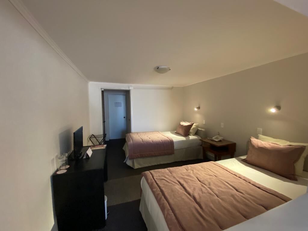 A hotel room with two beds, a desk, a chair, a TV, and a door leading to another room.