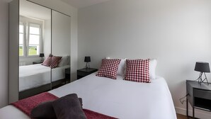 A modern hotel room with a large bed, checkered pillows, a mirror, and a nightstand with a lamp. - Farmhouse in Laigne Near Le Mans Circuit (Laigné-en-Belin)
