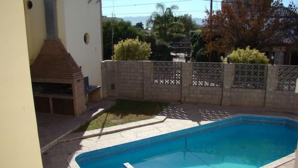 A rectangular swimming pool with a tiled deck, surrounded by a low brick wall and a decorative fence. - Hotel Temu (Villa Carlos Paz)