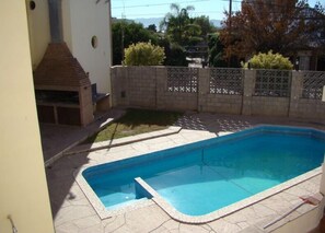 A rectangular swimming pool with a tiled deck, surrounded by a low brick wall and a decorative fence.