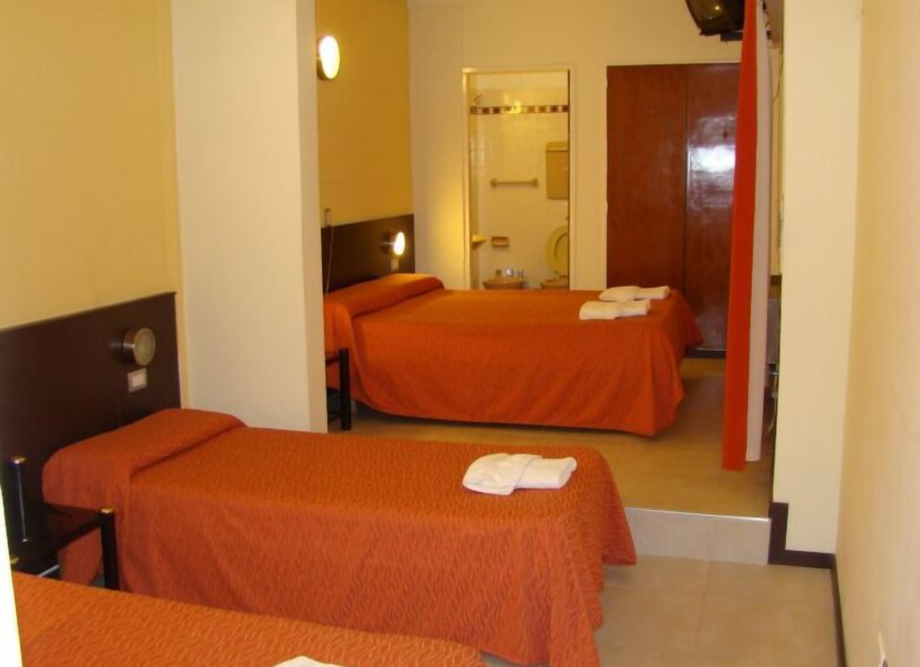 A hotel room with two single beds, a bathroom with a mirror, and a red door.