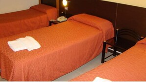 A room with three beds, each with an orange bedspread. There is a nightstand with a lamp and a telephone on one bed. - Hotel Temu (Villa Carlos Paz)