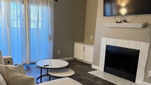 Una sala de estar con un sofá, chimenea, televisor y comedor con mesa y sillas.