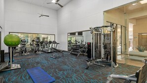 A gym with various exercise equipment, a blue mat, and a ceiling fan.