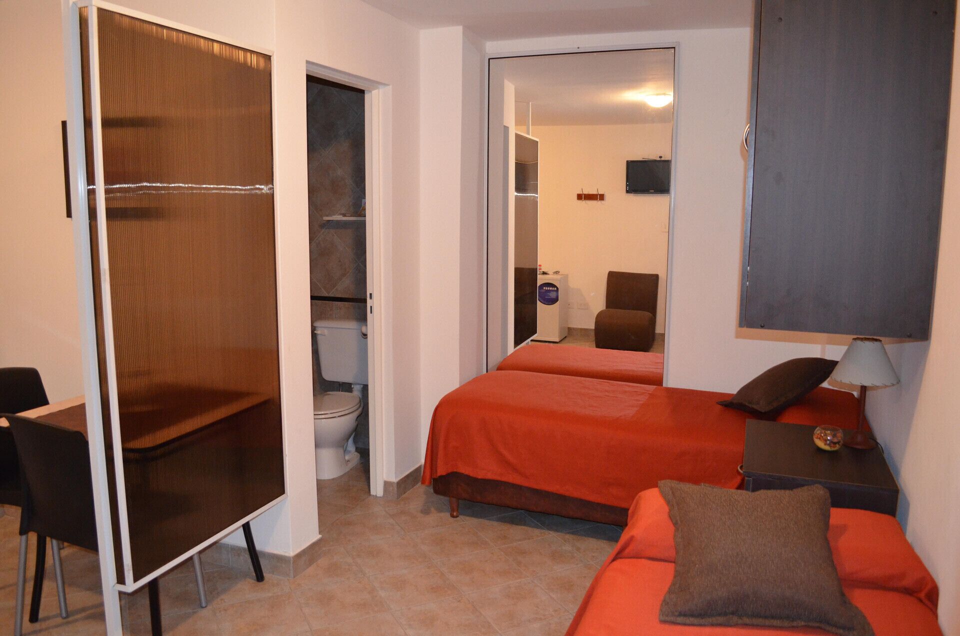 A compact hotel room with a single bed, a desk, a chair, and a wardrobe.