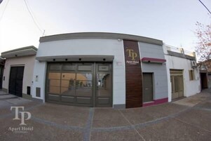 Un edificio moderno con fachada curva, un llamativo letrero de 'TP Apart Hotel' y una entrada amplia con puerta de vidrio.