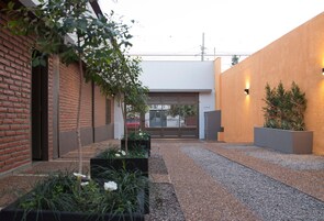 A courtyard with a gravel path, a brick building, a modern wall with a light fixture, and a garage door.