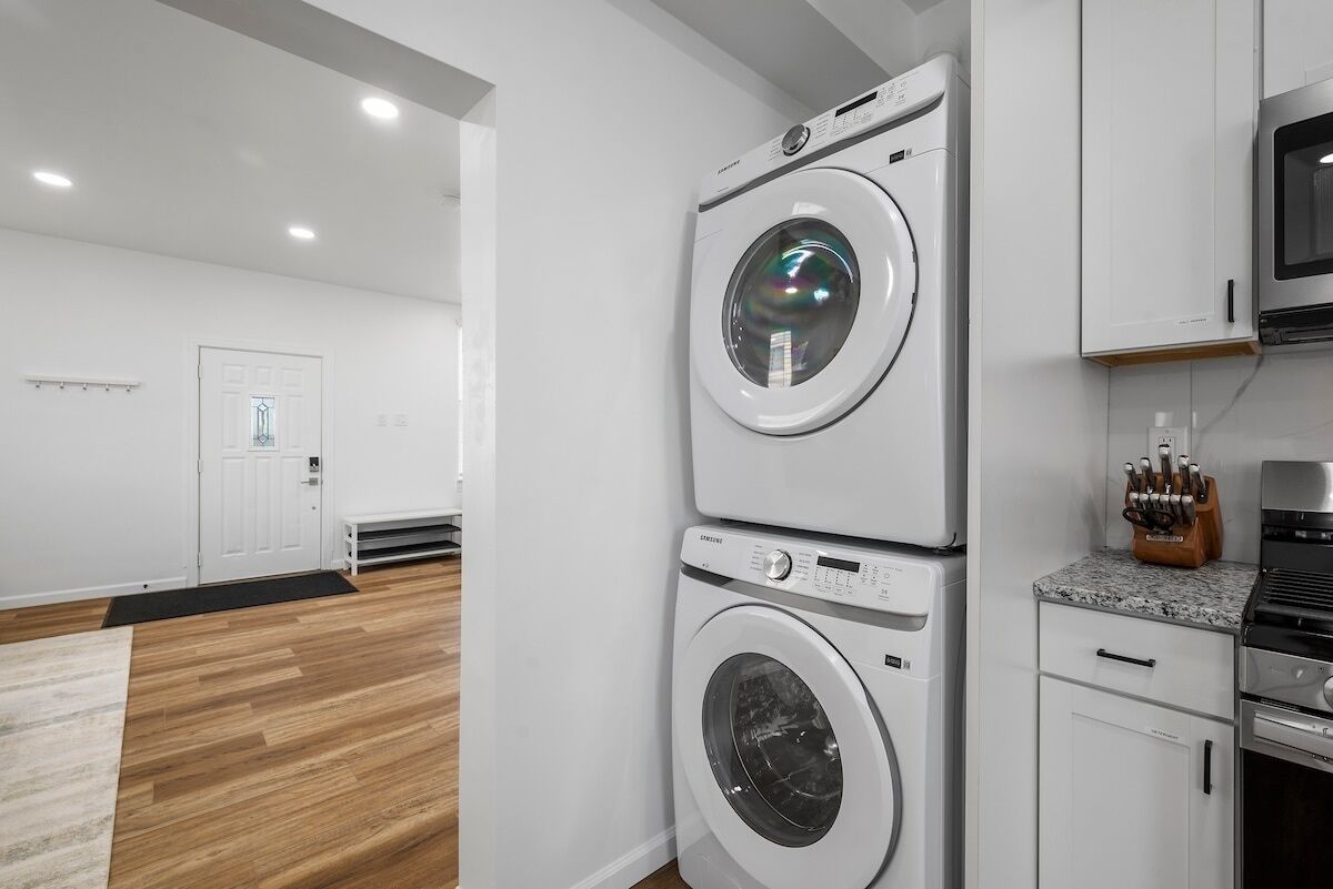 A laundry room with two stacked front-loading washing machines, a microwave, and a stove.