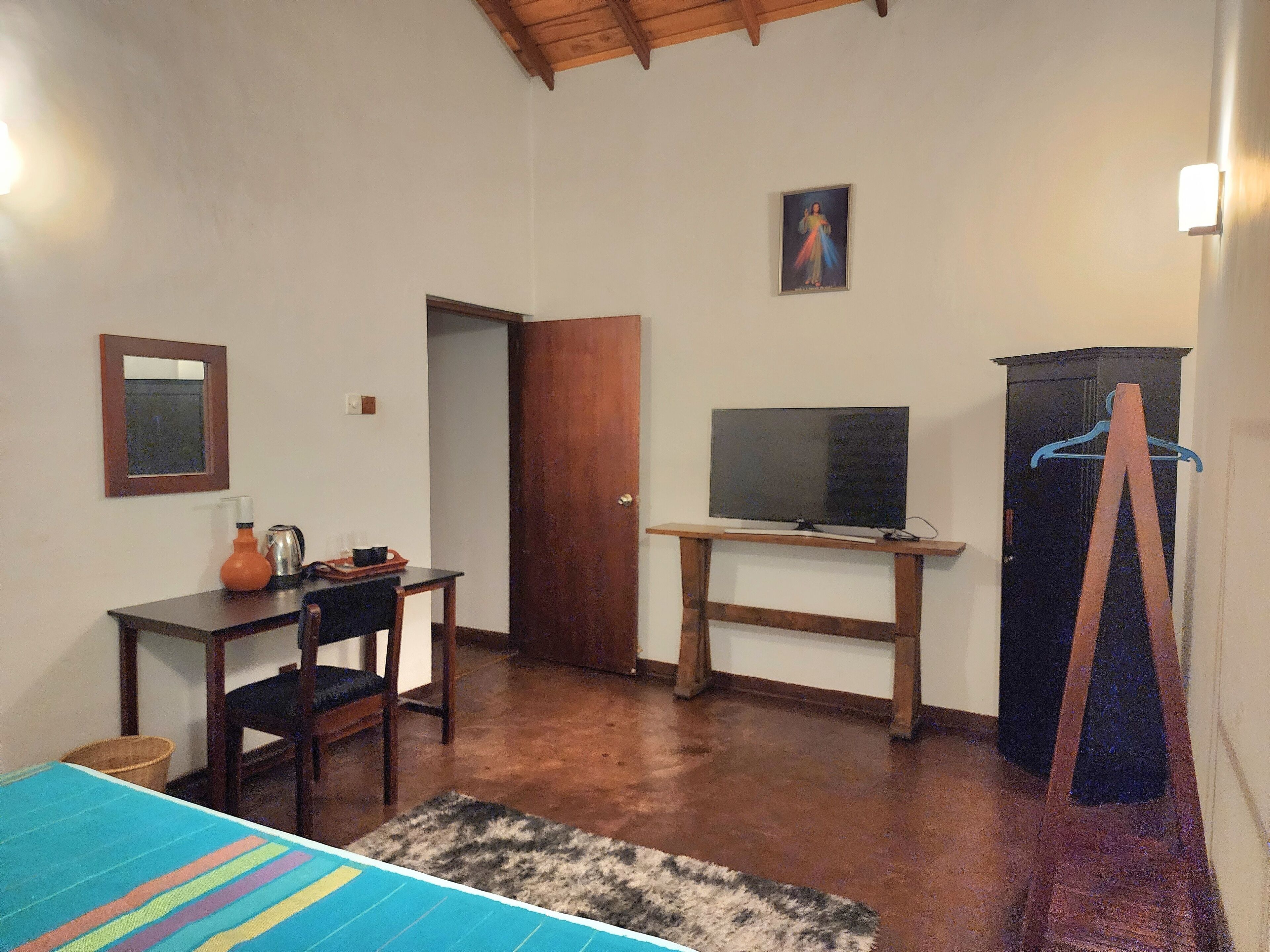 A room with a wooden desk, a television on a stand, a wardrobe, a mirror, and a door.