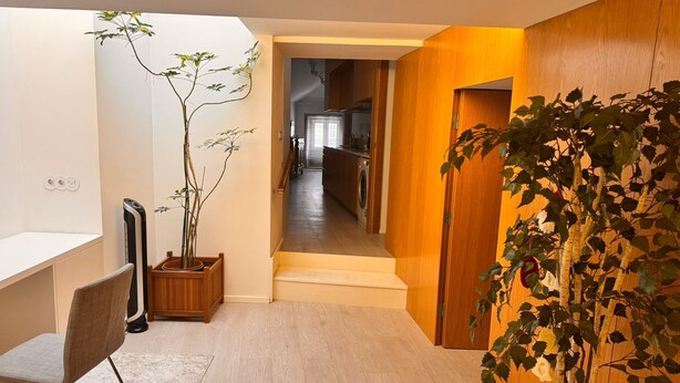 Un intérieur moderne avec un plancher en bois, un bureau avec une chaise, une plante en pot et une vue sur une cuisine et un coin repas.